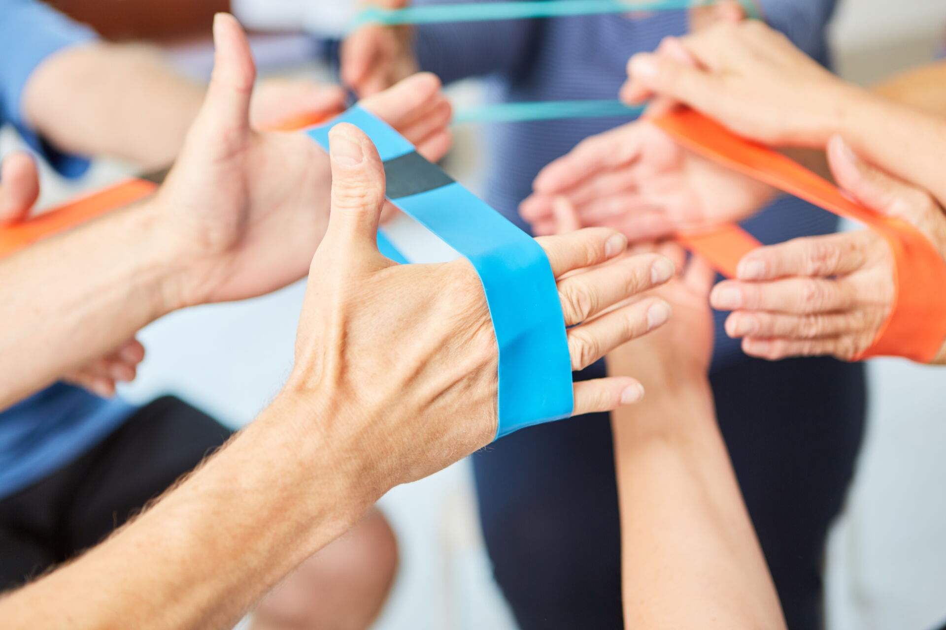 Patientenhände trainieren gemeinsam mit bunten Therapiebändern in der Praxis für Ergotherapie in motio.